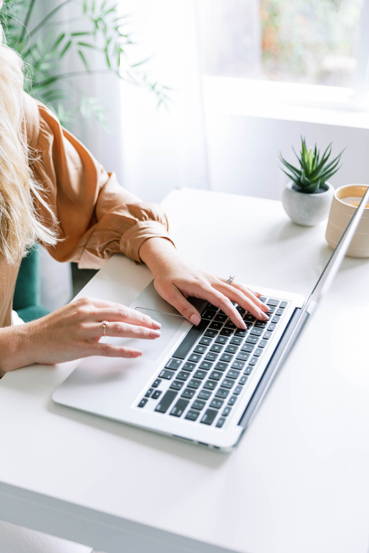 a woman is typing on her macbook at an aesthetic desk, decorated with a succulent